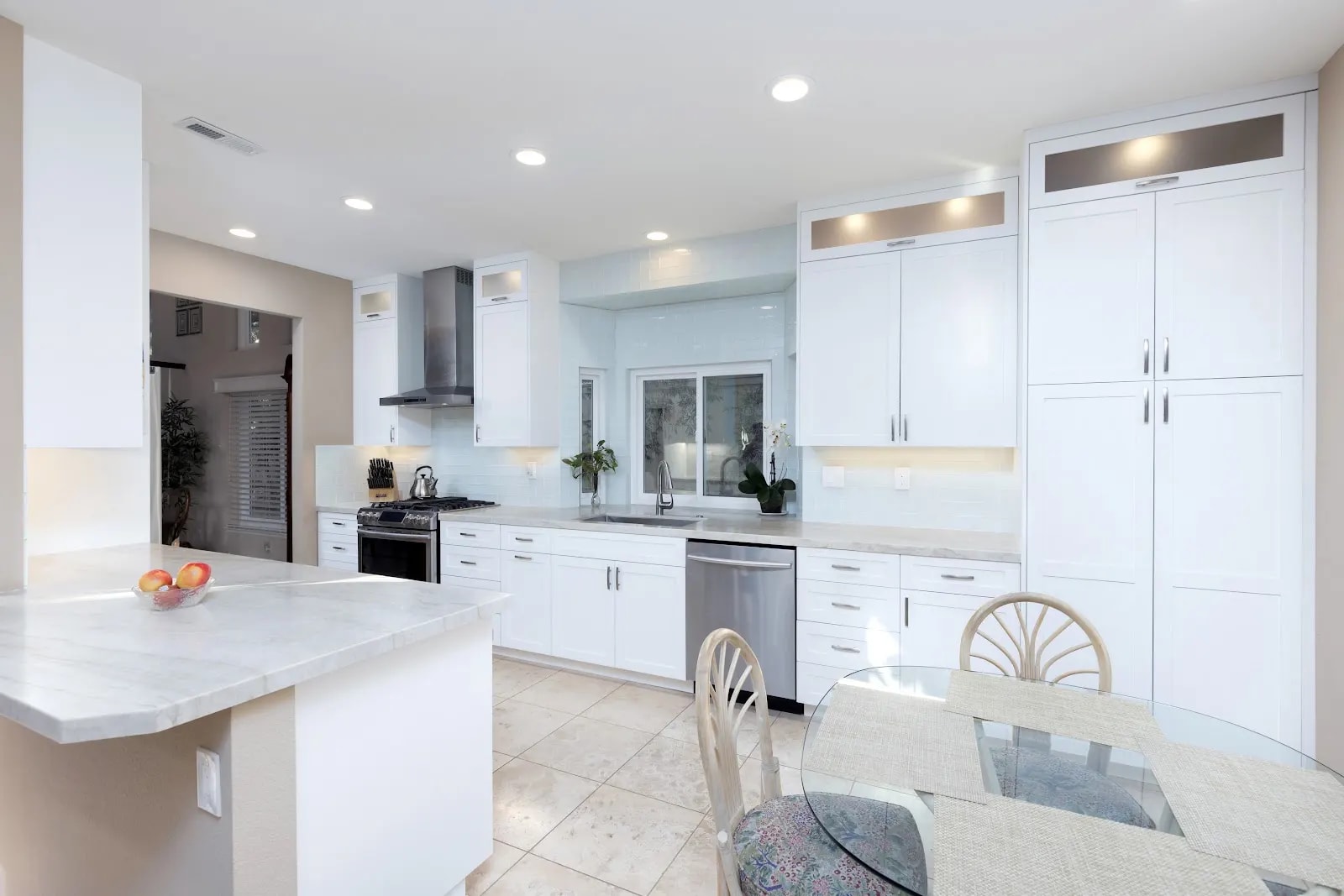 White kitchen cabinetry with illuminated upper cabinets, a peninsula and a breakfast table