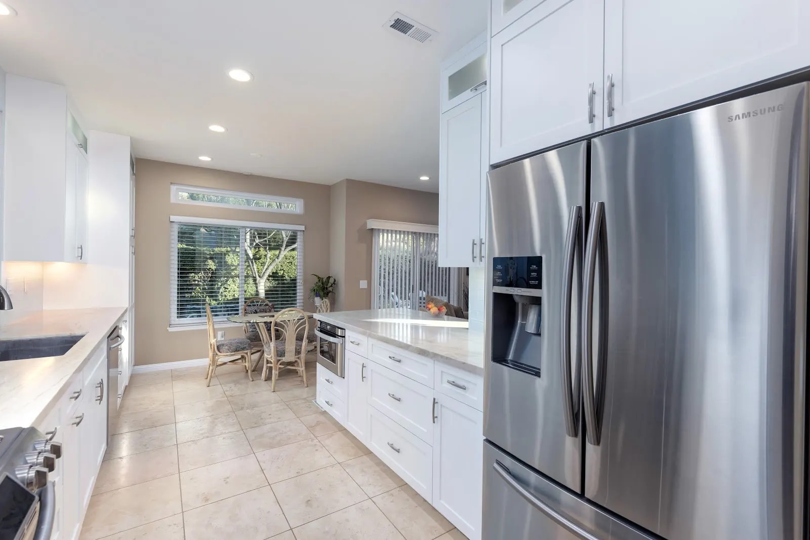 Kitchen walkway between white cabinets and a peninsula, opening to a breakfast area